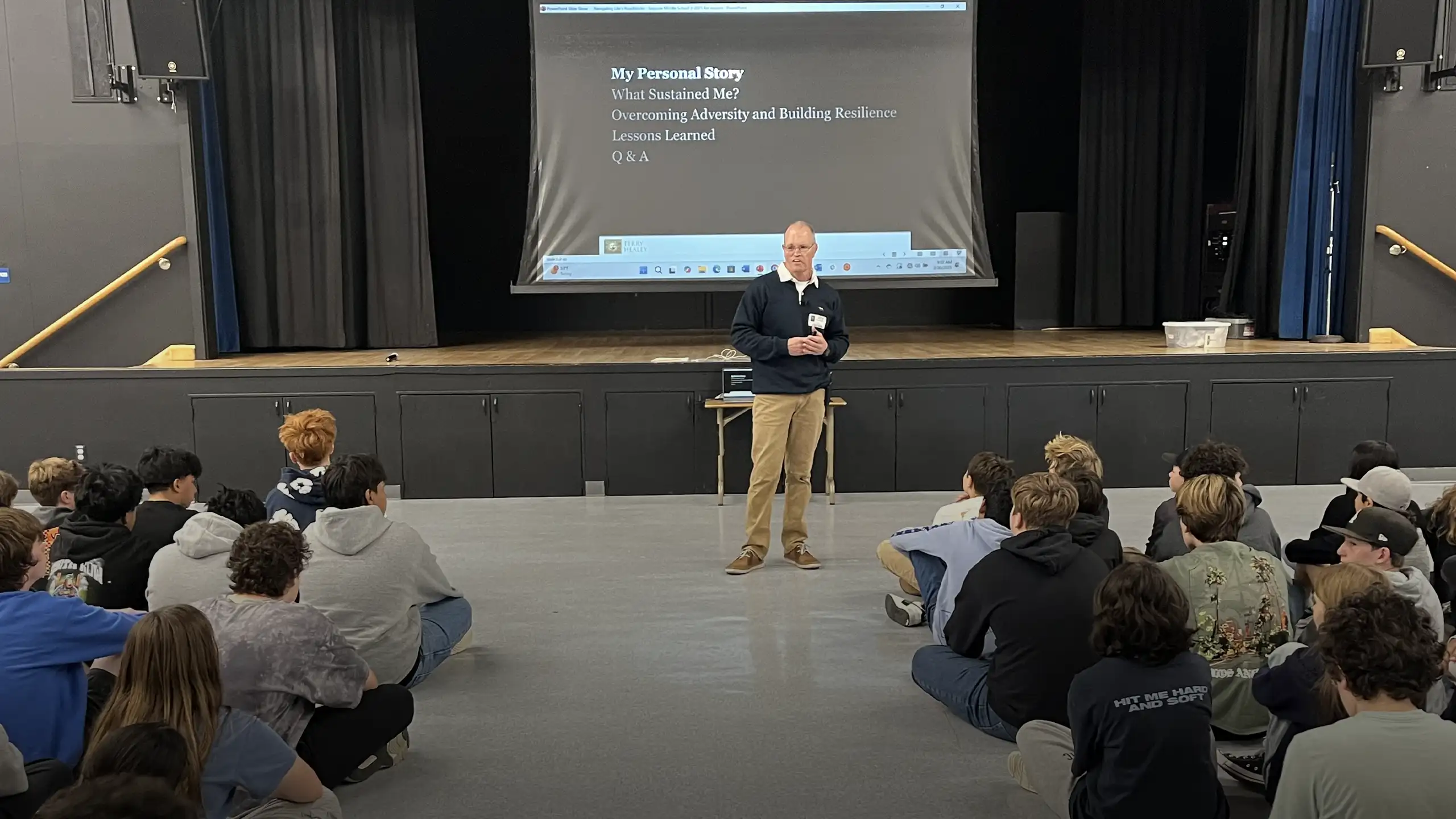 Terry speaking1 Motivational speaker on stage engages audience; presentation screen displays slide title.