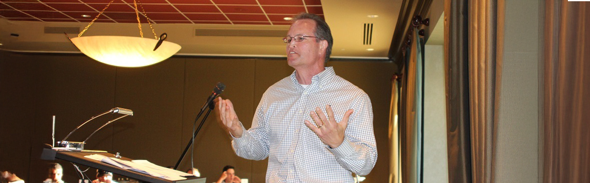 A motivational speaker addressing the audience from the podium in a conference room.